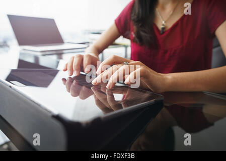 Closeup of hands of female computer technician sitting and typing on tablet computer with laptop in background Stock Photo