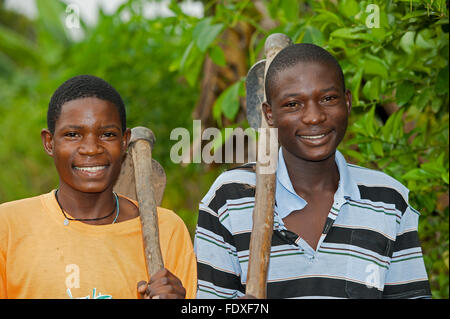 Two young men with hoes over their shoulders return home after a day working in fields. Uganda. Stock Photo