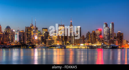 The mid-town Manhattan skyline remains illuminated with lights reflecting off the Hudson River before sunrise in New York City. Stock Photo