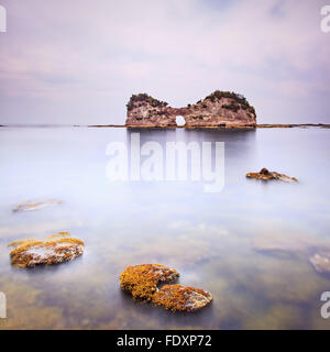 Hole island and rocks in a tropical blue ocean. Cloudy sky. Long exposure photography Stock Photo