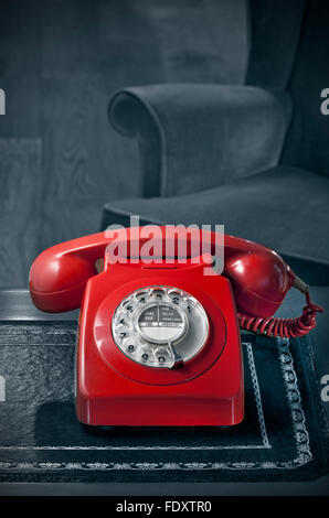 1970s old red dial telephone style fashion classic sales  retro office GPO BT red phone handset antique desk mono background & vintage chair Stock Photo