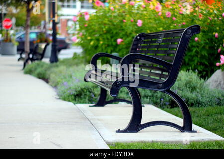 Black metal wrought iron park bench by colorful flowers in springtime park setting Stock Photo