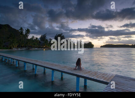 Woman sitting on jetty at sunset, Hauru Point, Mo'orea, Society Islands, French Polynesia