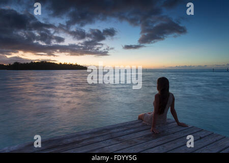 Woman sitting on jetty at sunset, Hauru Point, Mo'orea, Society Islands, French Polynesia Stock Photo