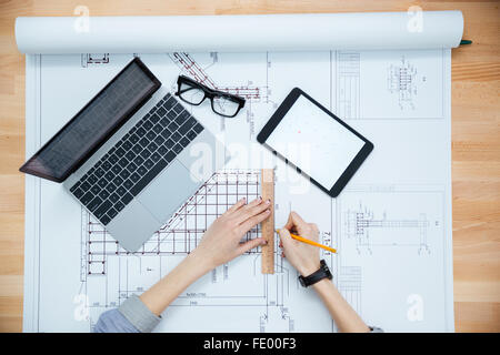 Top view of hands of female architect drawing blueprint and using laptop and tablet Stock Photo