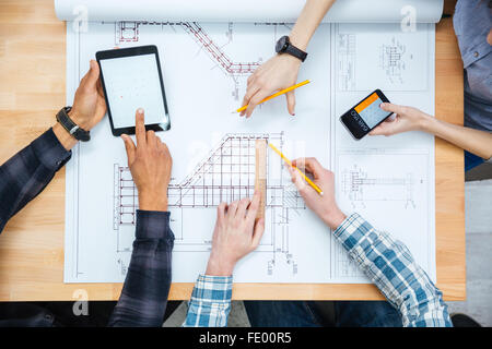 Multiethnic group of designers making calculations and working with blueprint using tablet and smartphone Stock Photo