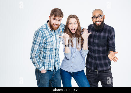 Beautiful amazed young woman standing and pointing on her two bearded handsome friends Stock Photo