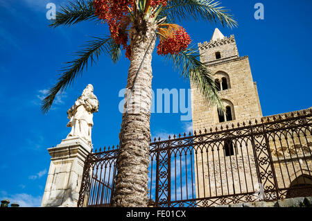 Low angle view of church tower and palm tree with religious statue in Cefalu city and comune in the Province of Palermo, Sicily, Stock Photo