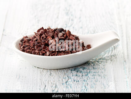 Cacao nibs in porcelain spoon on white wooden table Stock Photo