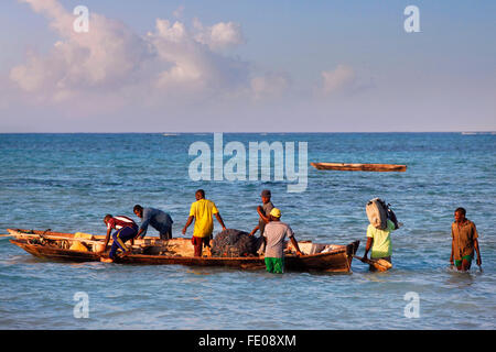 A dhow (traditional sailboat) in the background and a crowded fishing boat and fishman in the foreground in the Indian Ocean Stock Photo