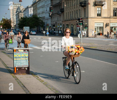 Young Danish woman cycling around town with bright flowers in her basket, on Dronning Louises Bro in sunny Copenhagen, Denmark Stock Photo