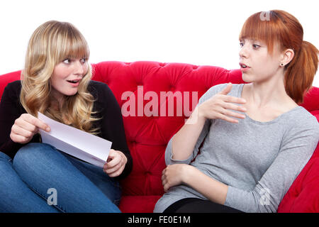 young beautiful blond and red haired girls on red sofa are excited about letter in front of white background Stock Photo