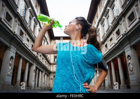 Now it is time to invest in your body and no matter you are at hometown or traveling. Sporty woman with headset is drinking wate Stock Photo