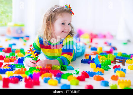 Cute funny preschooler little girl in colorful shirt playing with construction toy blocks building a tower in sunny kindergarten Stock Photo