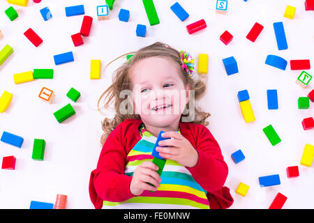 Cute funny preschooler little girl in colorful shirt playing with construction toy blocks building a tower in sunny kindergarten Stock Photo