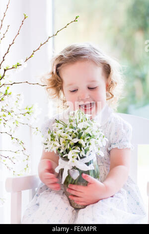 Little girl playing with first spring flowers at home. Child watering house plant. Toddler with cherry blossom tree Stock Photo