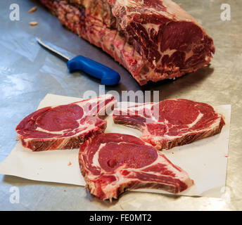 Three slices of raw rib eye steak over butcher paper sheet next to knife and meat section on metal table Stock Photo