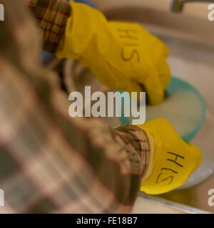 close shot of two gloved hands hand washing dishes with yellow gloves with HIS written on them Stock Photo