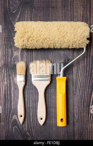Two paint brushes and roller on old wooden background