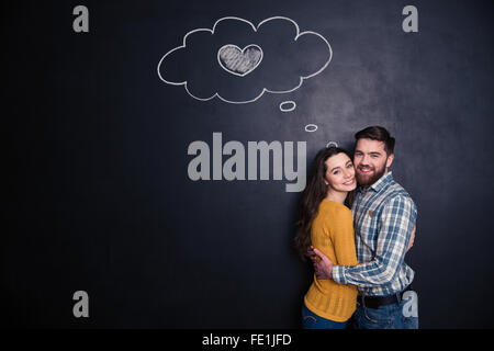 Smiling beautiful loving young couple standing and hugging  over background of chalkboard Stock Photo