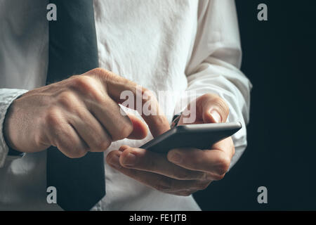 Young unrecognizable businessman professional texting on smartphone using message app in dark office interior. Stock Photo