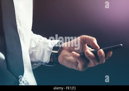 Young unrecognizable businessman professional texting on smartphone using message app in dark office interior. Stock Photo