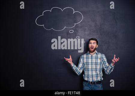 Confused angry bearded man shouting and standing on blackboard background Stock Photo