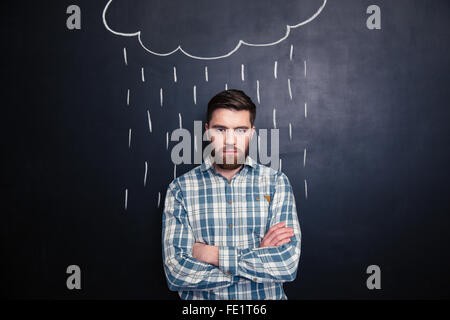 Serious handsome young man with beard standing with arms crossed under the drawn rain over background of chalkboard Stock Photo