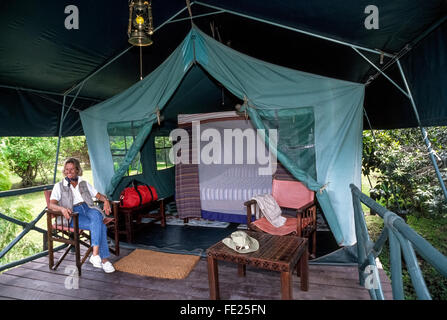 A female visitor relaxes on the covered porch of her outdoor tent accommodations that features a big bed protected by mosquito netting at a Masai Mara safari camp in Kenya, East Africa. Stock Photo
