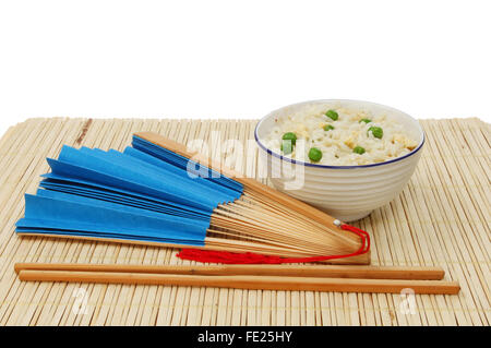 Asian meal, egg fried rice in a bowl with chopsticks and a blue paper fan on a bamboo matt against a white background Stock Photo