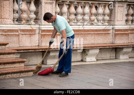 A daily early morning cleanup as a  council street cleaner using a wooden witch broom, cleans part of Piazza San Marco  ( St. Ma Stock Photo
