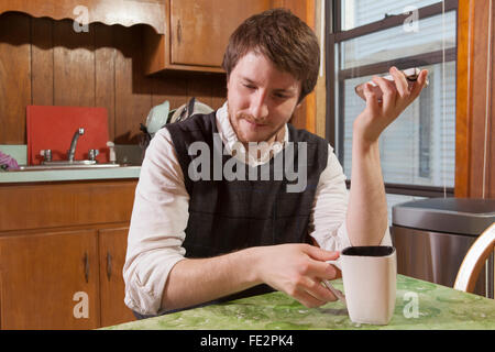 Blind man in his kitchen listening to assistive technology on his cell phone while having coffee Stock Photo