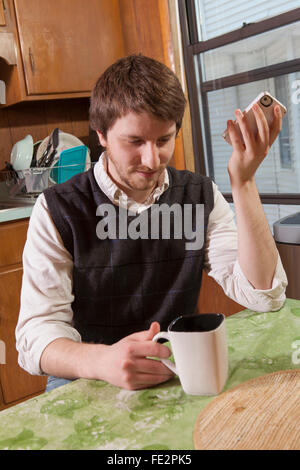 Blind man in his kitchen listening to assistive technology on his cell phone while having coffee Stock Photo