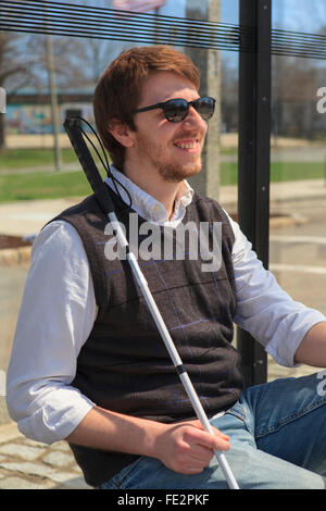 Young blind man with cane waiting at a bus stop Stock Photo