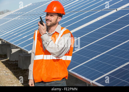 Power engineer standing at solar photovoltaic array and on radio Stock Photo