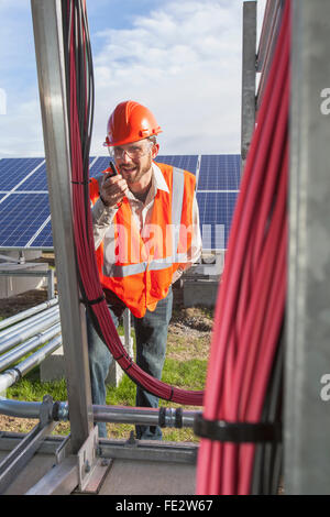 Power engineer talking on radio while looking at power cabling at solar photovoltaic array Stock Photo
