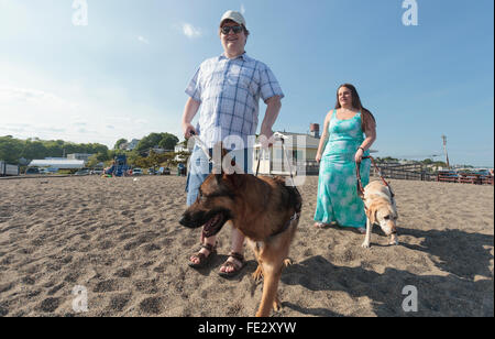 Blind couple with their service dogs walking along the beach Stock Photo