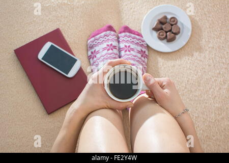 Girl having coffee in bed equipped with leisure accessories and snacks Stock Photo