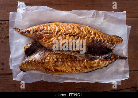 Smoked mackerel fillets on parchment paper against a rustic wooden background. Stock Photo