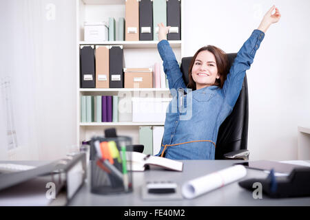 Happy Young Office Woman Sitting on her Chair Stretching her Arms While Looking at the Camera. Stock Photo