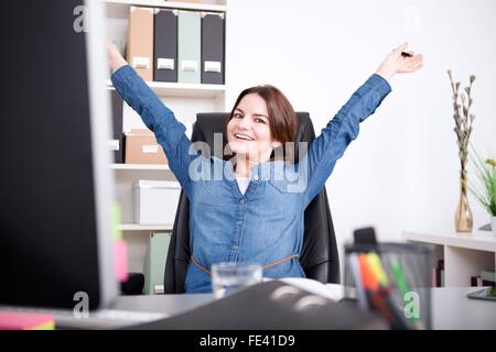 Happy Female Executive Sitting on her Chair at the Office While Stretching her Arms and Looking at the Camera. Stock Photo