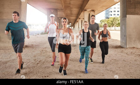 Healthy young people running together under a bridge. Group of young men and women doing running training. Stock Photo