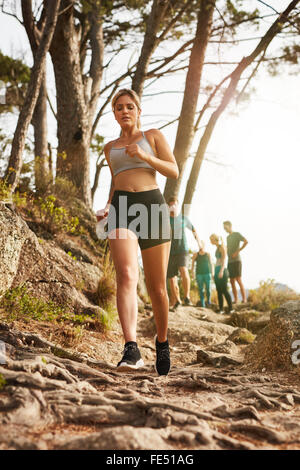 Image of fit young woman running outdoors. Woman trail runner training for cross country run with people in background. Stock Photo