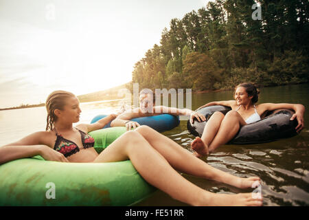 Portrait of young friends floating on lake with inflatable rings. Young people relaxing in water on a summer day. Enjoying their Stock Photo