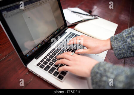 Person Tying on a Macbook with Notepad and Diary Stock Photo