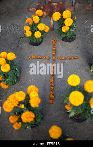 A cross made with yellow marigold flowers, known as cempasuchil, decorate a tomb at the cemetery in San Gregorio Atlapulco Stock Photo