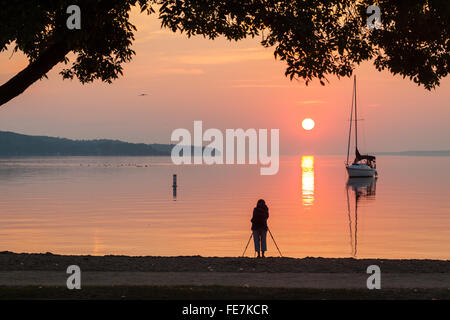 Waterfront scene of a Sailboat at sunrise, with a reflection in the water. Stock Photo