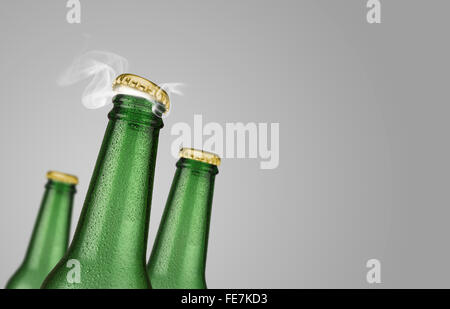 Horizontal photo of three green cold beer bottles with water drops and golden cap open on grey background Stock Photo