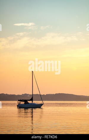 Waterfront scene of a Sailboat at sunrise, with a reflection in the ...