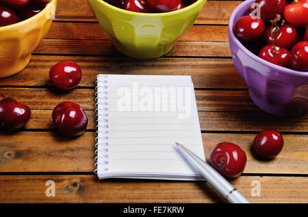 Colorful bowl with cherries and notebook on wooden table Stock Photo
